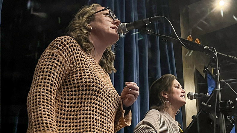 Two women in a duo singing on stage with microphones in center of the casino.